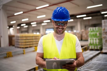 industry-worker-in-reflective-jacket-and-hardhat-looking-at-tablet-in-modern-factory-interior